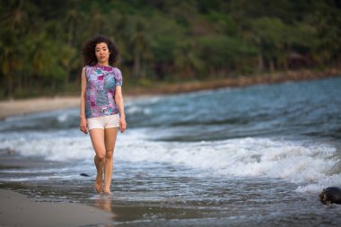 Deniz kıyısında yürüyen karışık ırktan bir kadın..