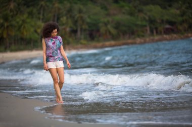 Sörf hattında melez bir kadın tropik bölgelerde deniz kıyısında yürüyor..