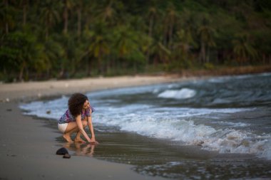 Melez bir kadın deniz kıyısında sörf çizgisinde oturur..