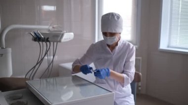 Diş muayenehanesinde masada oturan bir kadın diş hekimi anesteziyi hazırlar, şırıngayı iğneye batırır ve anestezi karpuzunu şırınganın içine sokar..