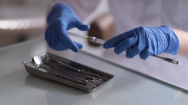 Kadın dişçinin elleri, diş muayenehanesinde, anesteziyi hazırlarken, şırıngayı iğneye batırırken, ve şırıngaya anestezi enjekte ederken..