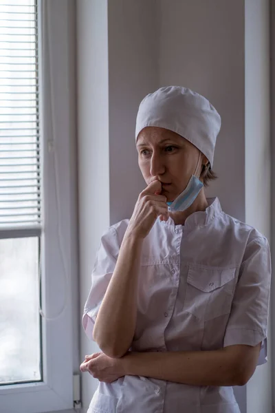Kvinnlig Läkare Med Mask Ansiktet Står Nära Fönstret Och Tittar — Stockfoto
