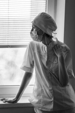 Pencereden bakan stresli bir kadın doktor. Siyah beyaz fotoğraf.