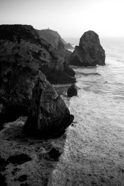 Günbatımında Atlantik Okyanusu 'ndaki kayalıkların ve sörfün en üst görüntüsü, Miradouro da Praia do Caneiro, Portekiz. Siyah beyaz fotoğraf.