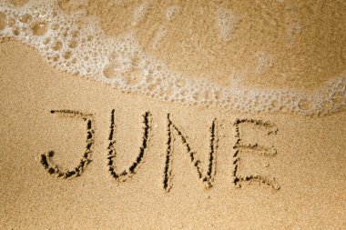 June - handwritten on the soft beach sand.