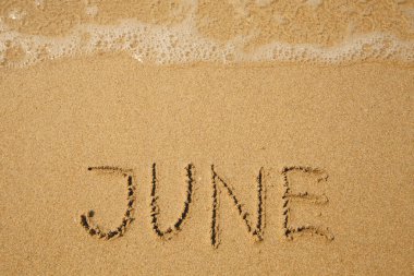June - handwritten on the soft beach sand.