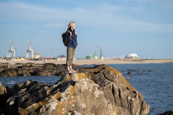 一名背着背包的女游客站在海港的海滨岩石上 — 图库照片