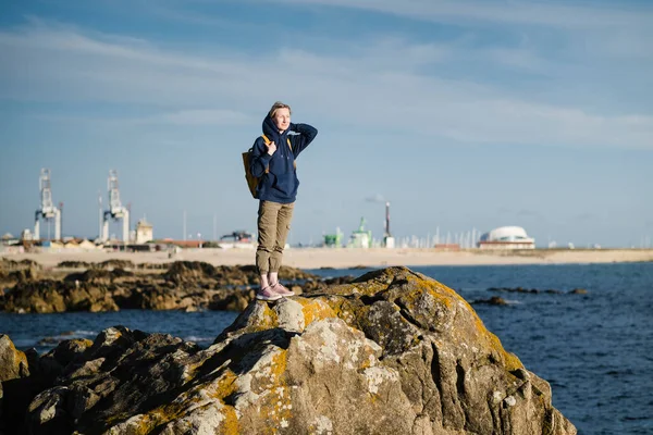 一个带着黄色背包的女游客站在港口的海滨岩石上 — 图库照片