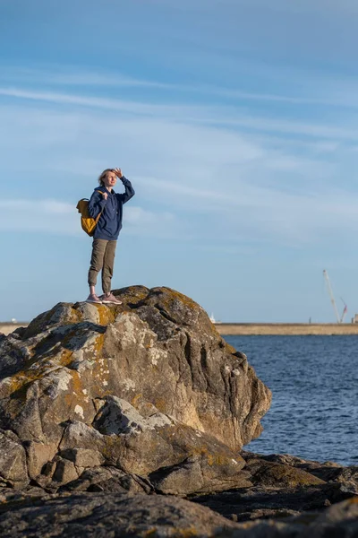 一个背着背包的女人站在沿海的海洋岩石上 — 图库照片