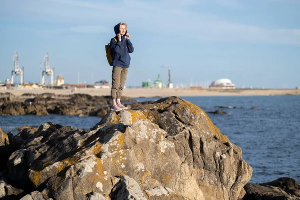 海港の海岸岩の上にはリュックを持った女性観光客が立っている ストック写真