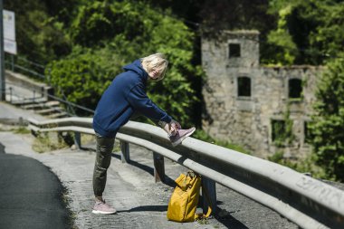 Sarı sırt çantalı bir bayan yürüyüşçü yolda bağcıklarını bağlıyor..