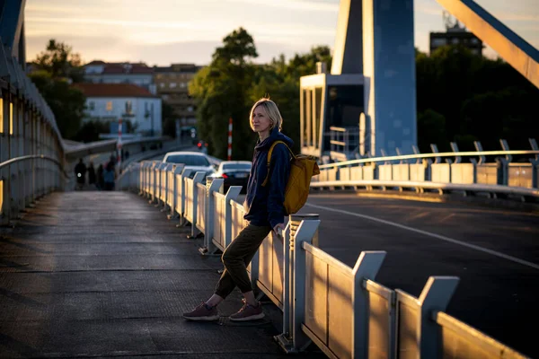 日落时 一只背着黄色背包的雌性站在一座金属桥上 葡萄牙波尔图 — 图库照片