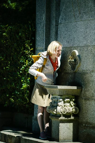 一个女游客喝中世纪的饮水机里的水 — 图库照片