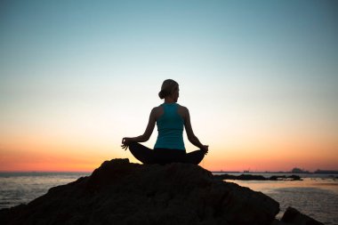 Kadın, gün batımında sahilde yoga yapıyor..