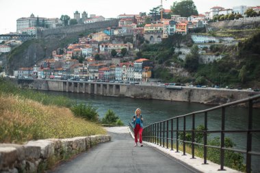 Dişi bir turist yorucu bir şekilde dağa tırmanır. Arka planda bulanık bir görüntü Portekiz 'in Porto şehrini gösteriyor..