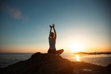 Güzel bir günbatımında okyanusta yoga yapan bir kadının silüeti..