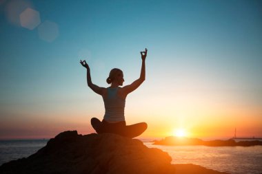 Silhouette of a woman doing yoga on the sea beach during a beautiful sunset.