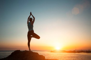 A woman does yoga and meditation on the sea beach during a beautiful sunset. 