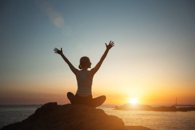 A woman does yoga, on a sea beach during a beautiful sunset. 