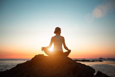Silhouette of a woman doing yoga in the lotus position on the beach during a beautiful sunset.  