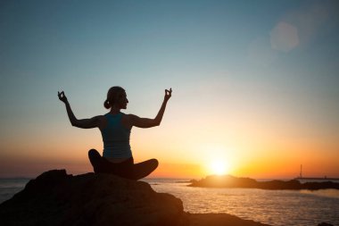 Silhouette woman yoga, meditating on the ocean beach during a beautiful sunset.   