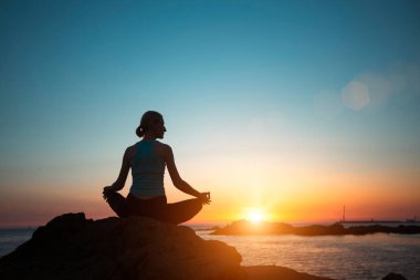 A woman does yoga, meditating on an ocean beach during a beautiful sunset.  