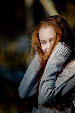 A golden-haired teenage girl poses in the park for a portrait.