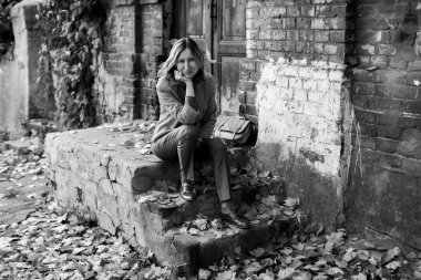 A graceful middle-aged woman sits on the steps of a brick house. Black and white photo.
