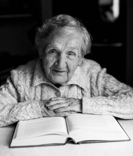 A portrait of an old lady reading a book in her own home. Black-and-white photo.