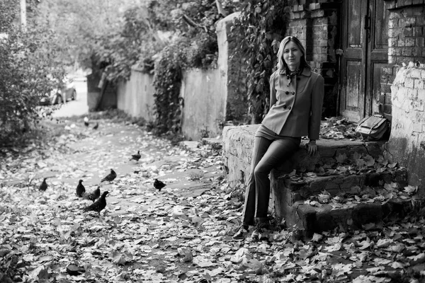 A graceful middle-aged woman sits on the steps of an old brick house. Black and white photo.