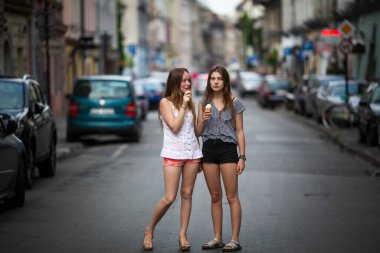 Two girlfriends are walking around town in the summer and eating ice cream. 