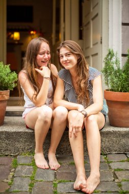 Two pretty girlfriends spend time on the stone steps of a house in the old town.