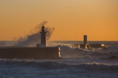 Alacakaranlıkta dalgalarla yıkanmış bir deniz feneri manzarası. Porto, Portekiz.