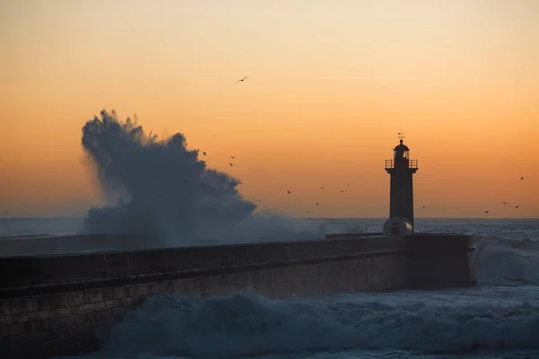 Lighthouse, washed in the sunset by a wave. Porto, Portugal.