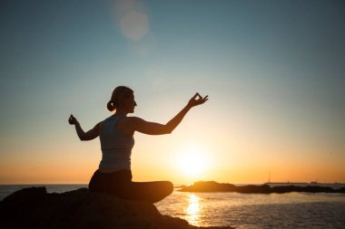 Yoga yapan kadın okyanus kıyısında gün batımında lotus pozisyonunda meditasyon yapıyor..  