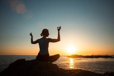 Okyanusta gün batımında yoga yapan bir kadının silueti..  