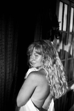 Bir kır evinin önünde havluya sarılı uzun saçlı bir kadının portresi. Siyah beyaz fotoğraf.