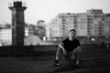 Deniz fenerinin yanındaki sette genç bir adam oturuyor. Siyah beyaz fotoğraf.