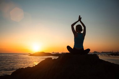Yoga yapan kadın silueti, güzel bir gün batımında okyanus sahilinde meditasyon yapıyor..   