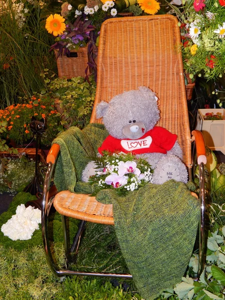 Een mooie teddybeer in een schommelstoel-stoel onder planten in de tuin tentoonstelling in Moskou. augustus, 2013. — Stockfoto