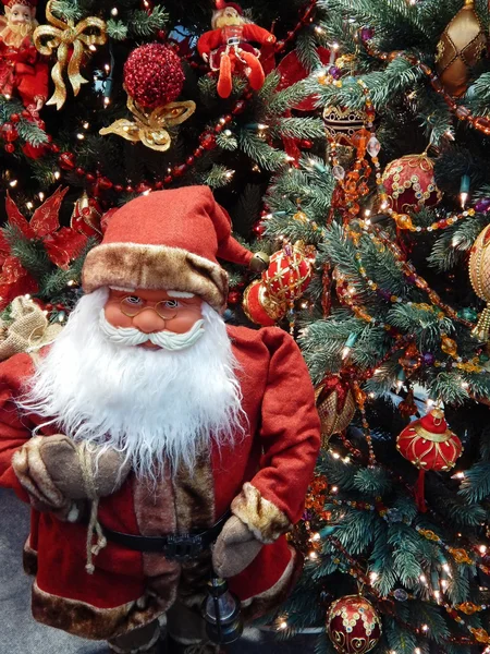 Игрушка Санта-Клаус с фонариком и мешок с подарками возле елки . — стоковое фото