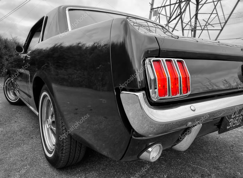 Iconic rear light cluster of a 1966 Mustang coupe.  Black and white with the light picked out in red