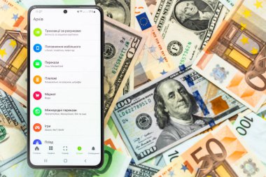 Kyiv, Ukrayna - 1 Aralık 2021: Mobil bankacılık Privat24 başvurusu ile akıllı telefon ekranı ABD doları ve euro banknotları geçmişi