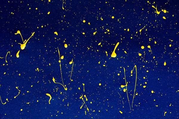 closeup of yellow paint drops on blue paper background for design purpose