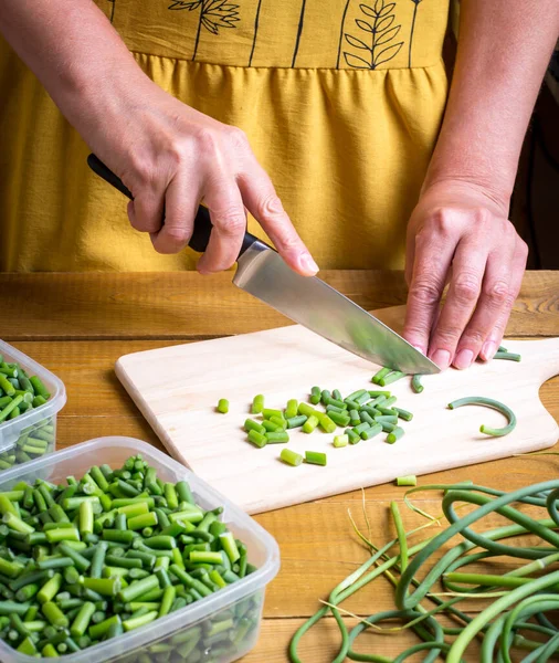 Flechas de ajo verde se cortan con un cuchillo en una tabla de madera. Preparación de alimentos para el invierno. — Foto de Stock