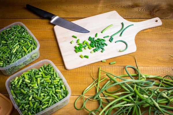 Flechas de ajo verde se cortan con un cuchillo en una tabla de madera. Preparación de alimentos para el invierno. — Foto de Stock