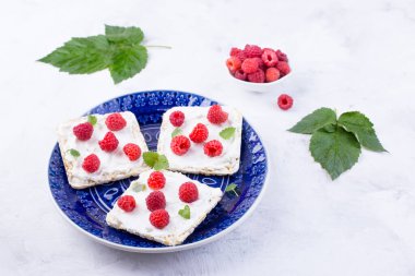 Krem peynirli tost ve mavi tabakta taze ahududu. Kahvaltı için lezzetli bir yaz yemeği. Yakın plan..