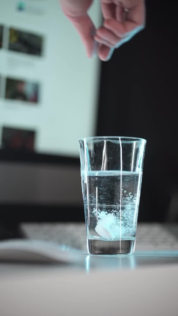 Το δισκίο πέφτει σε ένα ποτήρι νερό. αναβράζον δισκίο ασπιρίνη. κοντινό πλάνο σε φόντο χώρου εργασίας — Αρχείο Βίντεο