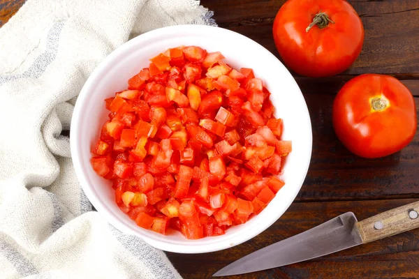 Raw chopped and diced tomatoes cubes in ceramic bowl over rustic wooden table. top view