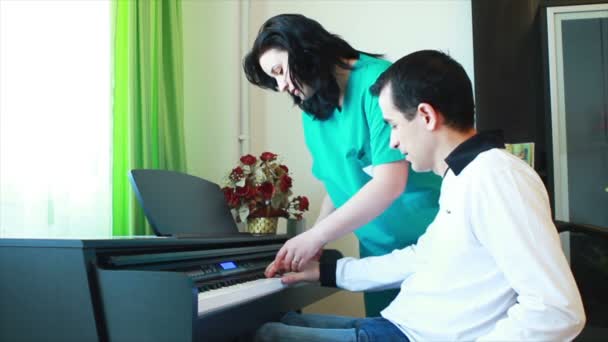 Therapy for young man in wheelchair using piano — Stock Video